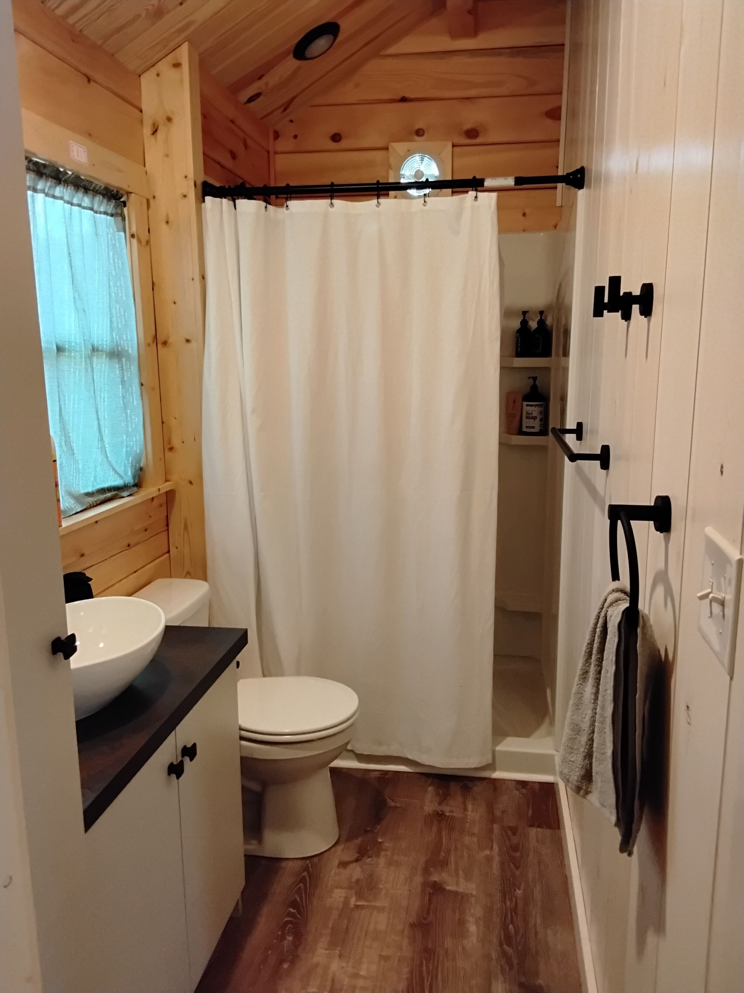 A wooden cabin bathroom with a white sink, toilet, and shower curtain.