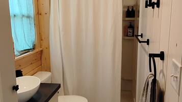 A wooden cabin bathroom with a white sink, toilet, and shower curtain.