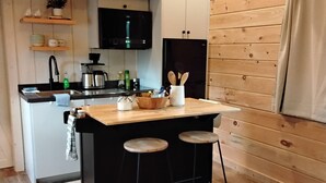 A compact kitchen with a wooden island, black bar stools, and a black refrigerator. - Serenity at Nottely River (Murphy)