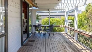 A wooden deck with a table and chairs, a pergola, and a view of greenery.