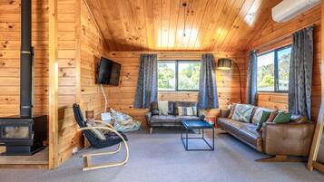 A cozy cabin interior with a fireplace, seating area, and large windows.