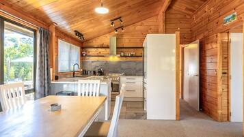 A wooden cabin interior with a kitchen, dining area, and a view of the outdoors.