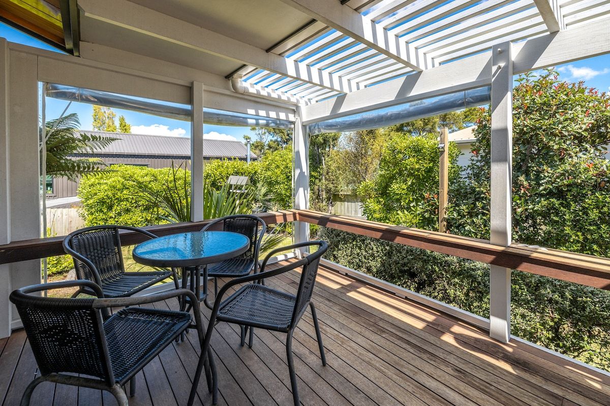 Un espace extérieur abrité, doté d’une terrasse en bois, d’une rambarde en métal et d’une table ronde avec des chaises.