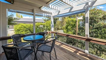 A covered outdoor area with a wooden deck, metal railing, and a round table with chairs.