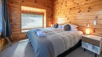 Una habitación con paneles de madera, una cama, un ventanal, una mesita de noche y una lámpara.