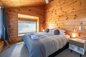 A wooden-paneled room with a bed, a window, a nightstand, and a lamp.