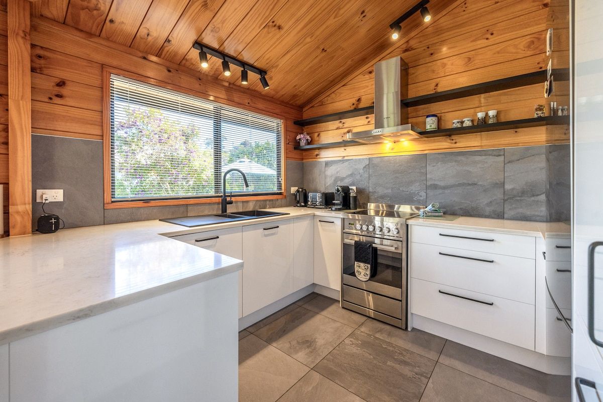 A modern kitchen with white cabinetry, a stainless steel oven, and a window with blinds.