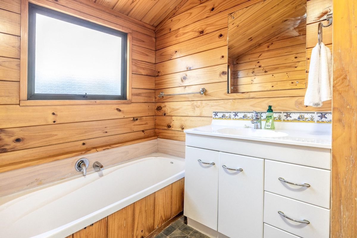A wooden cabin bathroom with a bathtub, a sink, and a window.