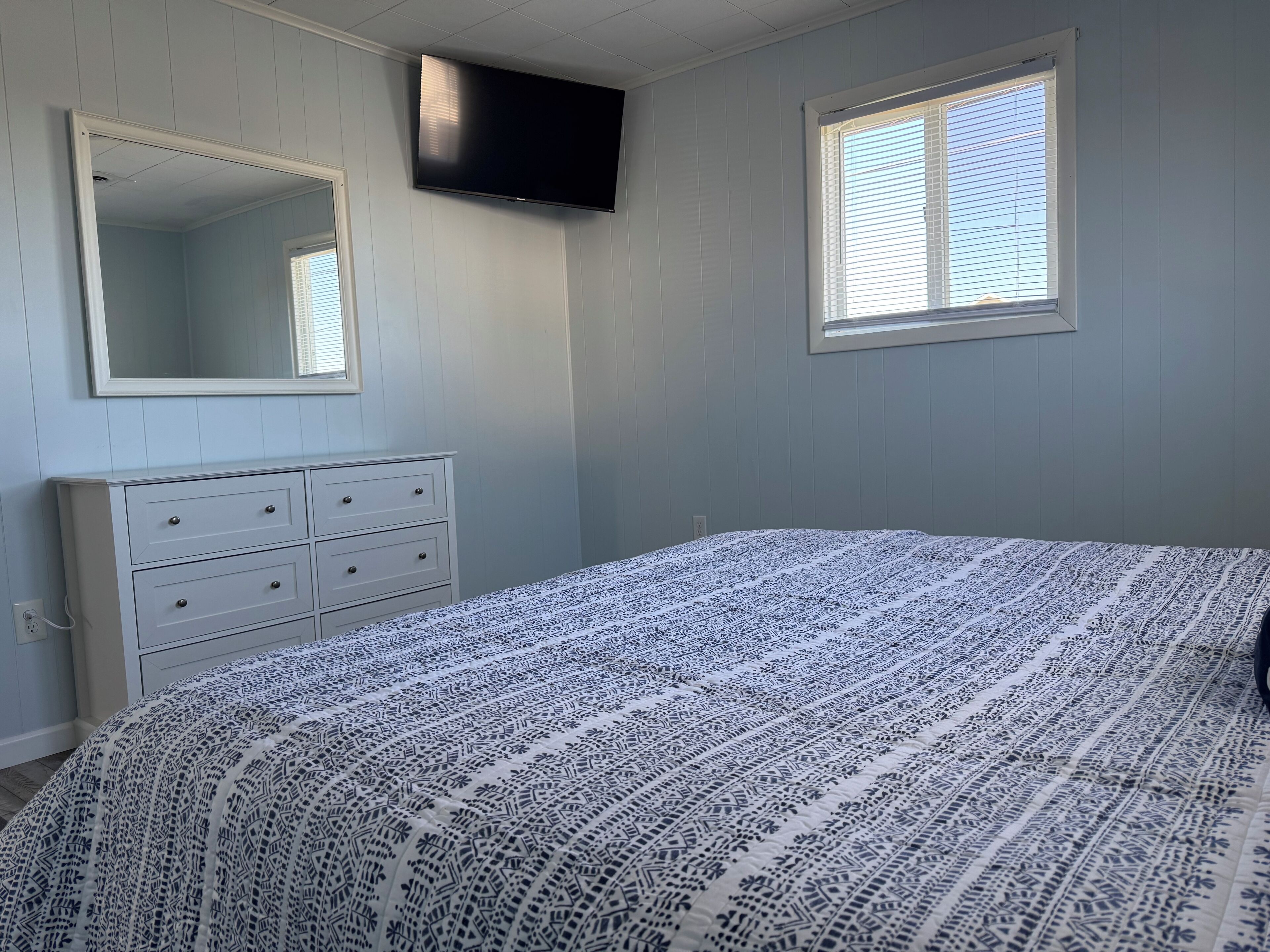 A bedroom with a bed, a dresser, a television, and a window.