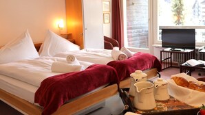 A hotel room with a bed, a TV, a window with a view, and a tray with breakfast items.