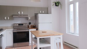 Een moderne keuken met grijze kastjes, een roestvrijstalen oven, een witte koelkast en een houten tafel.