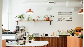 Een moderne koffiezaak met een houten toonbank, diverse koffieapparaten en een menukaart aan de muur met verschillende koffiesoorten.