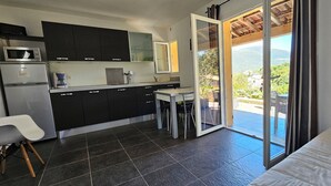 Een moderne keuken met donkere kastjes, een magnetron en een koelkast. Er is een kleine tafel met stoelen en uitzicht op een balkon met een zwembad.