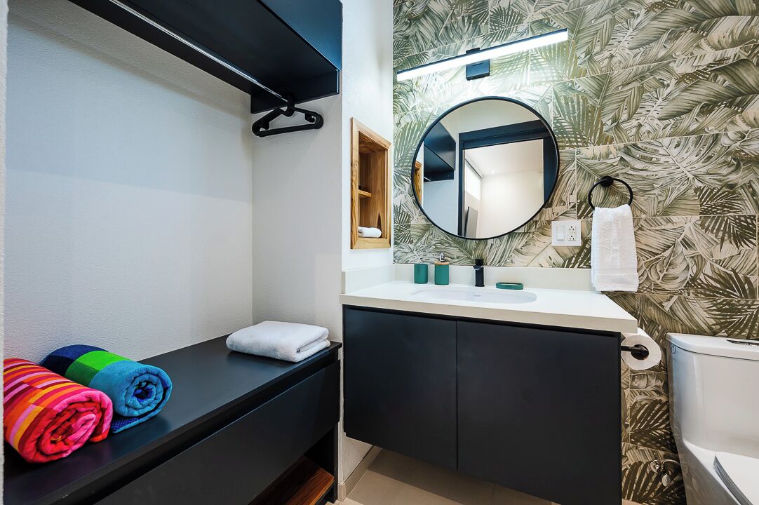 A bathroom with a round mirror, a towel rack, a small shelf with toiletries, and a toilet.