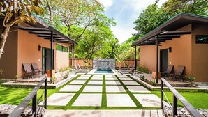 A modern outdoor patio with a pool, two lounge chairs, and a stone wall. - Private Tropical Villa with Backyard • Pool • Fast WiFi • Self Check-In (Provincia de Guanacaste)