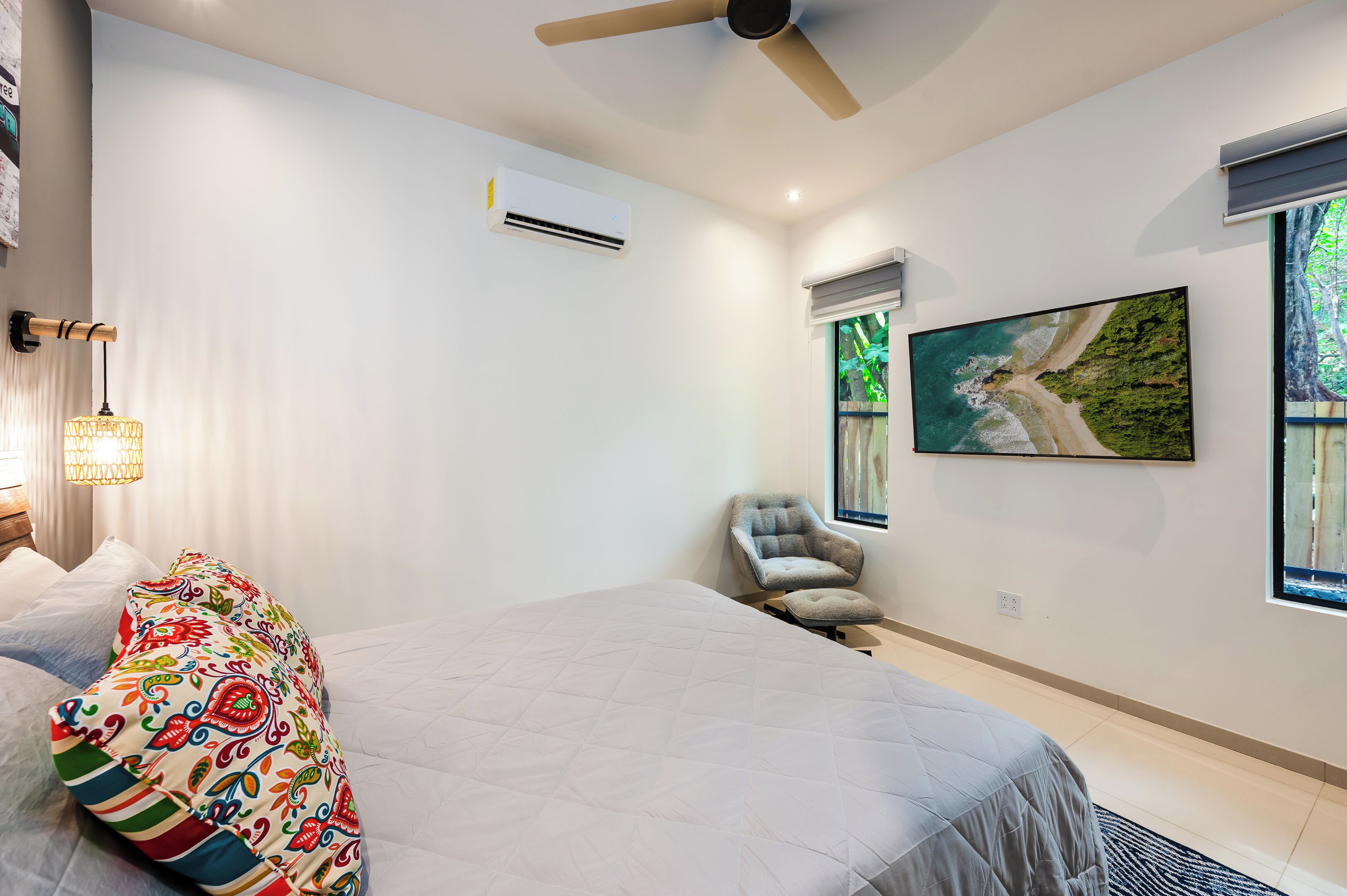 A modern bedroom with a large bed, a chair, an air conditioning unit, and a painting on the wall.