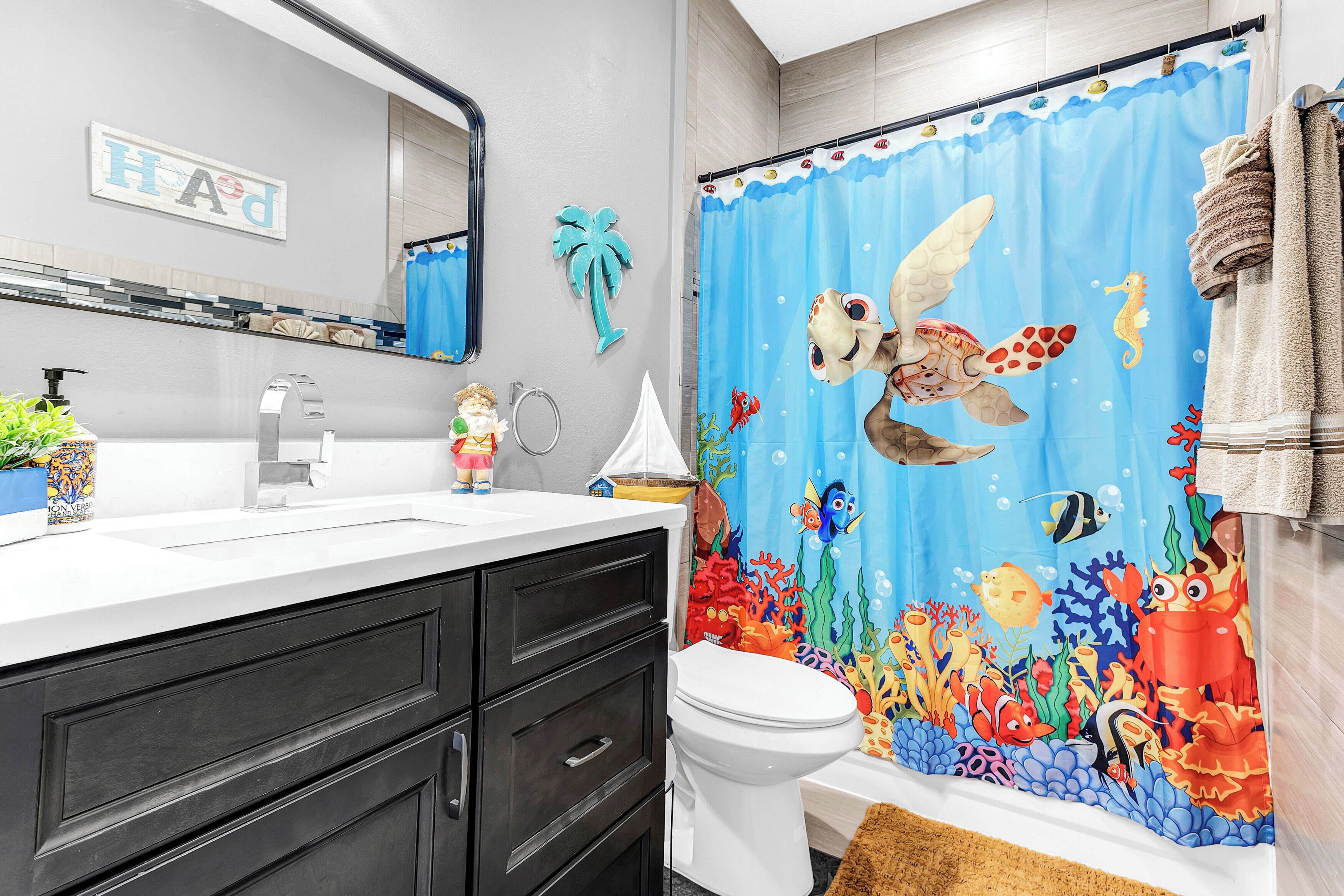 A bathroom with a white sink, dark cabinets, a toilet, and a shower curtain with a marine theme.