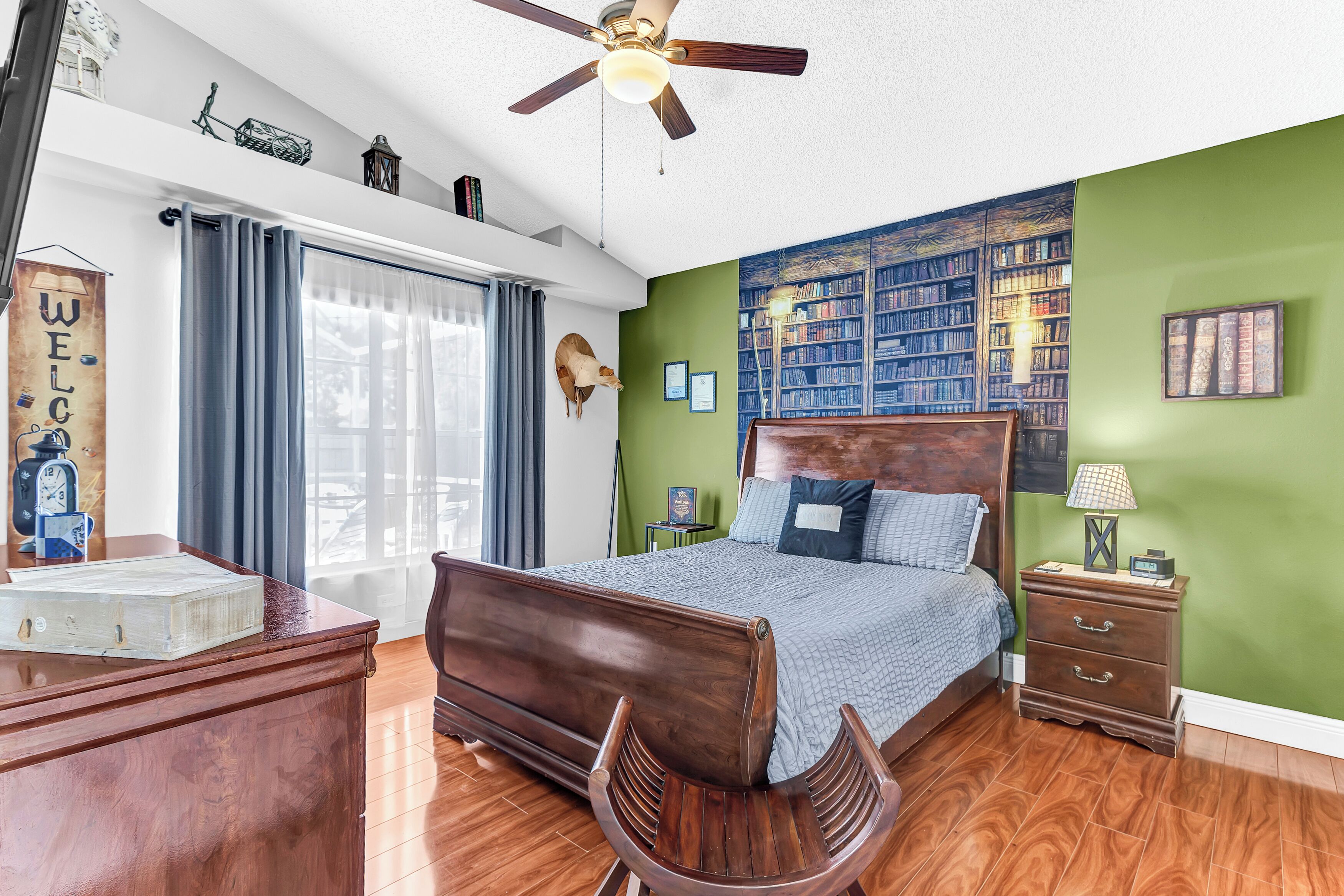 Una camera da letto con un letto in legno, una scrivania, una sedia, una libreria e una ventola a soffitto.