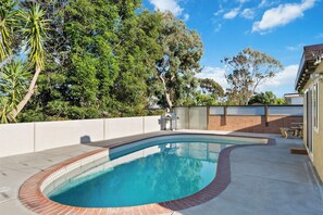 A swimming pool with a curved edge, surrounded by a brick border and a low white wall.