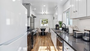 A modern kitchen with white cabinets, a central island, and a dining area with chairs.