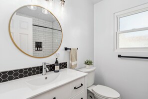 A bathroom with a white sink, a round mirror with a gold frame, a black soap dispenser, and a white toilet.