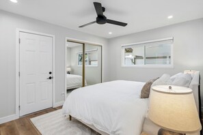 A bedroom with a bed, a ceiling fan, a window, and a door.