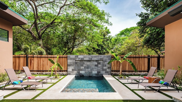 A rectangular swimming pool with a stone wall in the center, surrounded by lounge chairs and a wooden fence. - Private Tropical Compound • Exclusive Pool • 2 Villas • Fast WiFi (Provincia de Guanacaste)