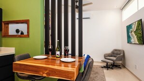 A dining area with a wooden table, two chairs, a bottle of wine, and a framed picture on the wall. - Private Tropical Compound • Exclusive Pool • 2 Villas • Fast WiFi (Provincia de Guanacaste)