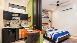 A compact room with a kitchenette, a bed with a striped bedspread, a ceiling fan, and a window with a view. - Private Tropical Compound • Exclusive Pool • 2 Villas • Fast WiFi (Provincia de Guanacaste)