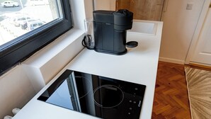 A kitchen with a black induction cooktop, a coffee maker, and a window overlooking a parking area.