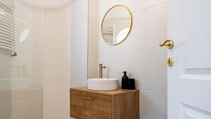 A bathroom with a wooden vanity, a white sink, a gold faucet, a black soap dispenser, and a gold-framed mirror.