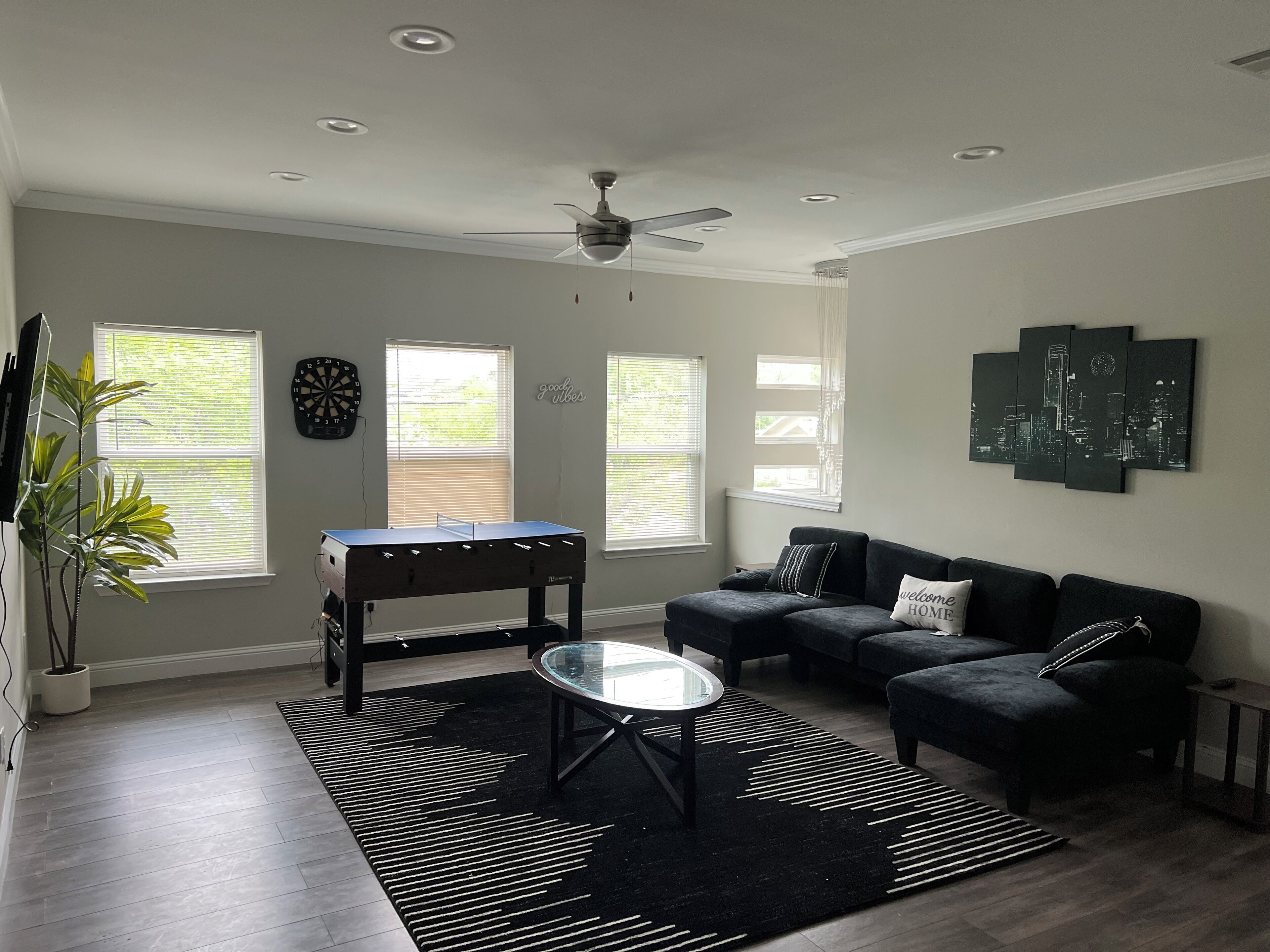Ein modernes Wohnzimmer mit einem Tischfußballtisch, einem Glastisch und einem dunkelgrauen Sofa.