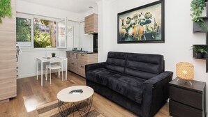 A modern living room with a black sofa, a small round table, a white dining table, and a kitchen area with wooden cabinets. - Immogroom-Renovated studio-AC-5min from the beach (Cannes)