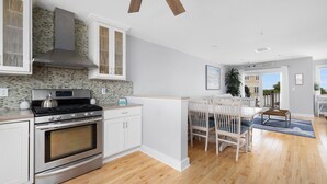 A modern kitchen with white cabinetry, a stainless steel stove, and a large oven. There is a dining area with a wooden table and chairs.