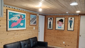 A room with a black leather sofa, wooden walls, and ceiling, and a door. - 1-bedroom apartment in the rear suite of the Howard Finster Vision House Museum. (Summerville)