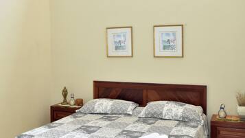 A bedroom with a large bed, two framed pictures on the wall, and a nightstand with a lamp.