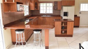 A kitchen with wooden cabinets, a central island with stools, a refrigerator, and a window. - Forest Villa near Zamorano & Uyuca Reserve (Tatumbla)