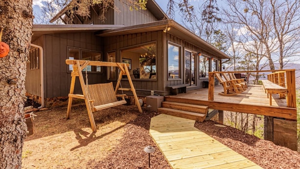 A wooden deck with outdoor seating, a swing, and a view of a mountain.