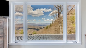 A window with a view of a wooden deck and mountains.