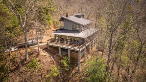 A two-story cabin with a deck, surrounded by forest.