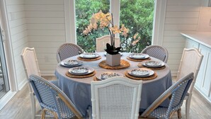 Mesa para seis personas dispuesta con sillas de mimbre, un jarrón de flores y vistas a la vegetación exterior.