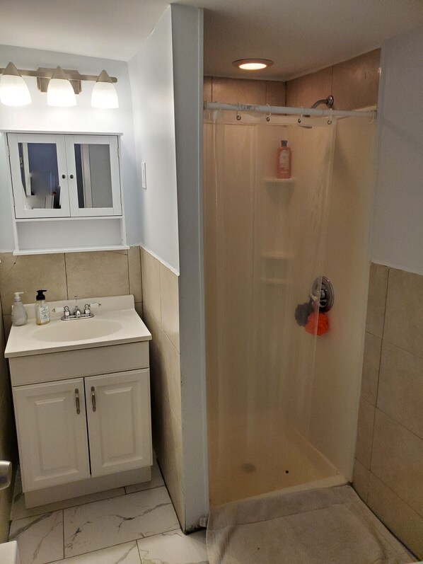 Une salle de bain avec un lavabo blanc, un miroir et des armoires, une douche avec une porte en verre et un sol carrelé.