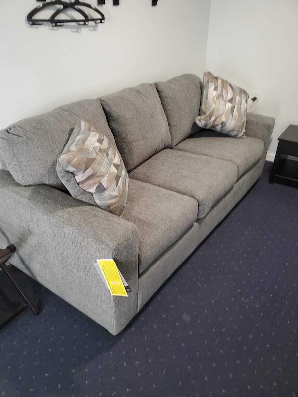Un canapé gris avec une étiquette, un coussin décoratif à motifs et une petite table d’appoint noire.