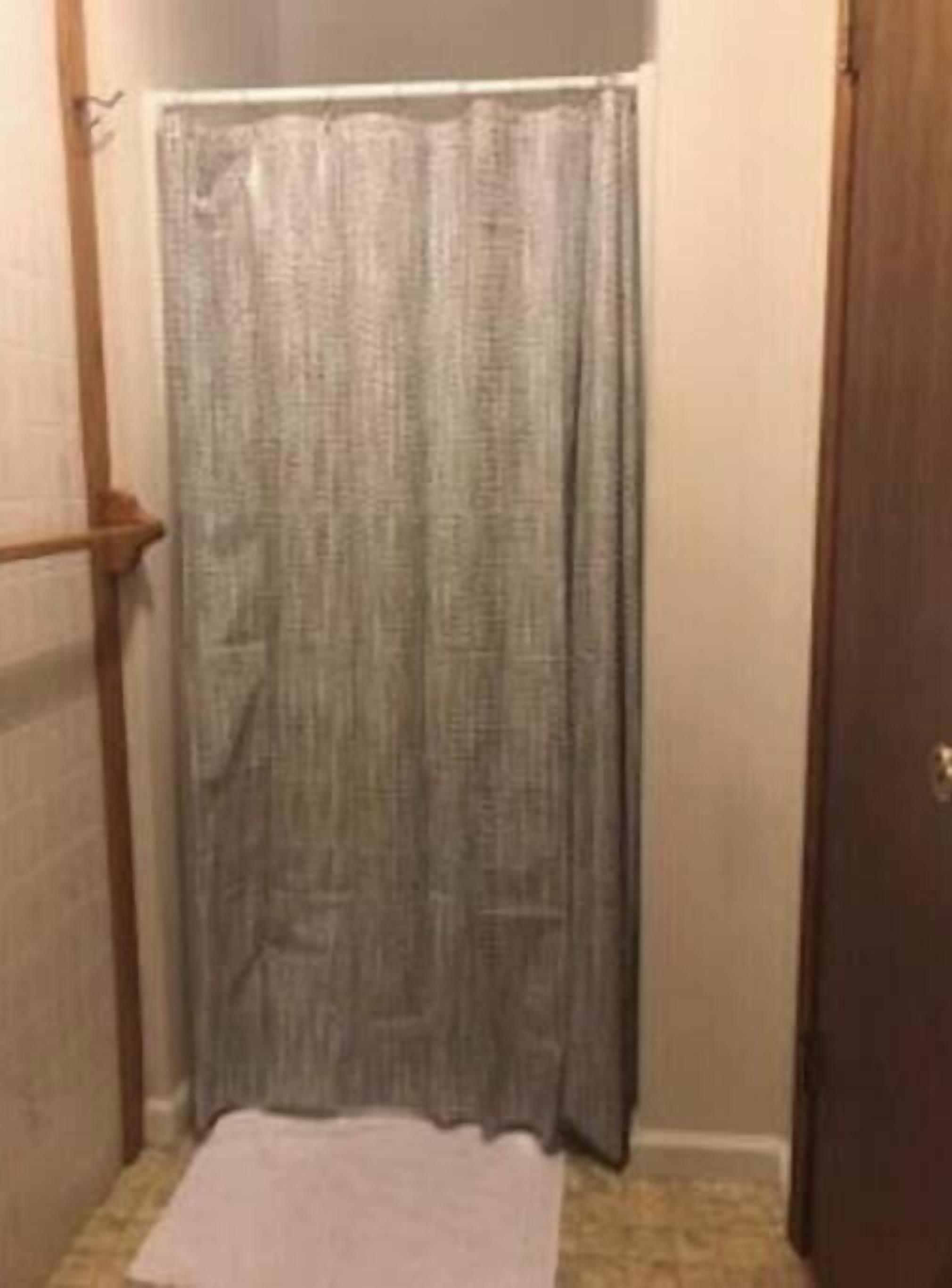 A bathroom with a shower curtain, a towel on the floor, and a wooden door.