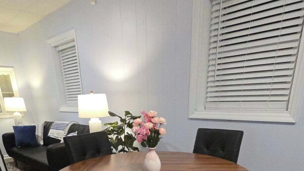 Une table de salle à manger ronde en bois, avec des chaises, un vase de fleurs et une lampe sur une table d’appoint.