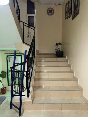 Una escalera con baldosas color crema, barandilla de metal negro y una planta en maceta en la parte superior.