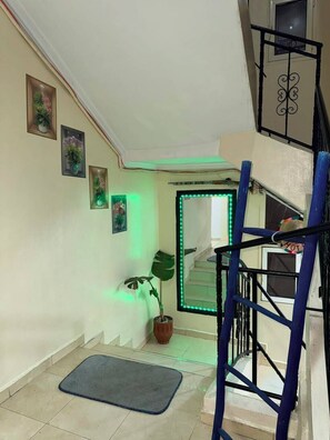 Una escalera con barandilla azul, una planta en maceta y un marco de puerta iluminado en verde.