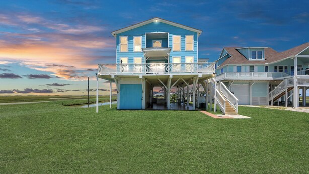 A two-story house with a balcony, a covered entryway, and a staircase leading to a garage. - Spacious deck 5-bedroom home in Freeport with WiFi, 3 full baths sits on canal. (Freeport)