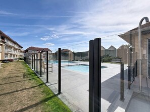 A swimming pool with a clear sky, surrounded by a paved walkway and a grassy area.