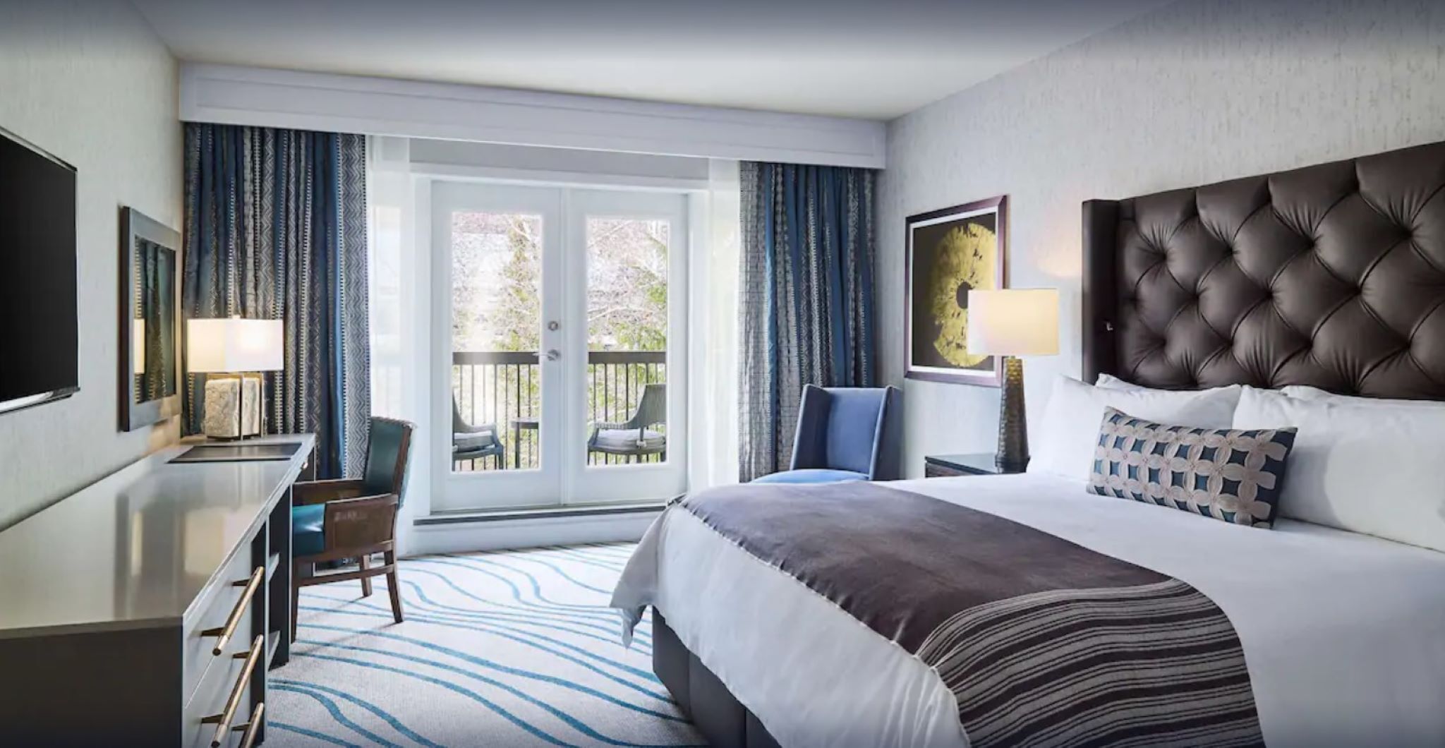 Une chambre d’hôtel comprenant un lit, un bureau, une chaise, un balcon avec vue et une fenêtre avec des rideaux.